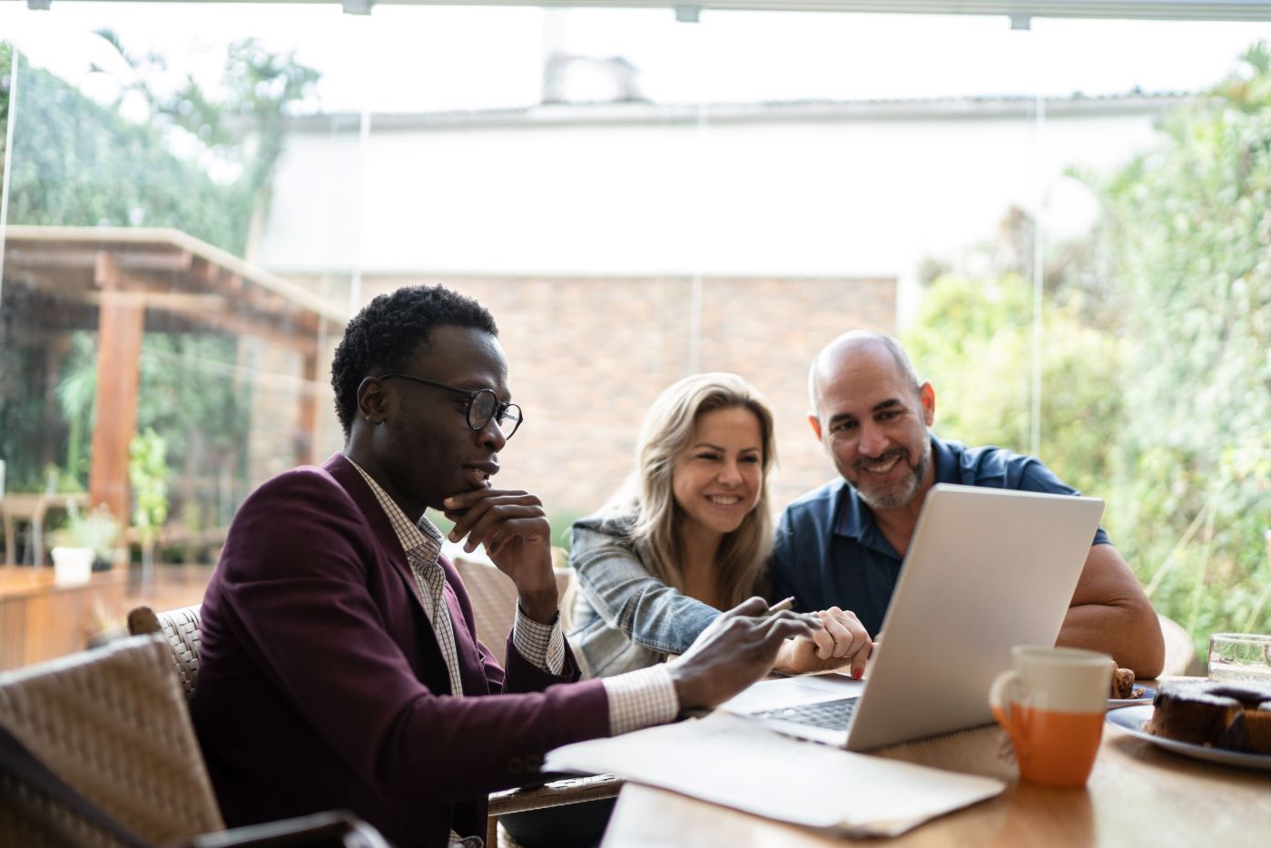 Three people sitting together looking at a laptop with papers and a drink on their desk